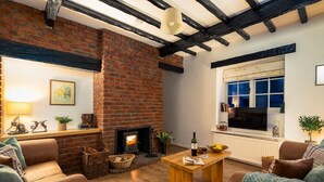 A cozy living room with a brick fireplace, wooden furniture, and a large window. - Cosy Yew Tree Cottage With Scenic Field Views (Scarborough)
