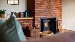 A cozy room with a brick fireplace, a bookshelf, and a wicker basket. - Cosy Yew Tree Cottage With Scenic Field Views (Scarborough)