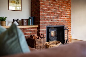 A cozy room with a brick fireplace, a bookshelf, and a wicker basket. - Cosy Yew Tree Cottage With Scenic Field Views (Scarborough)