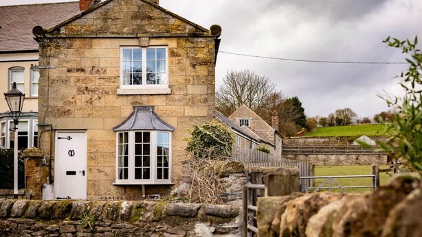 A stone building with a white door and window, surrounded by stone walls and a grassy field. - Cosy Yew Tree Cottage With Scenic Field Views (Scarborough)