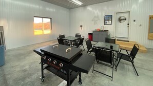 Ett rymligt inomhusområde med ett stort bord, stolar, en grill, en diskho och en dörr med en välkomstskylt.