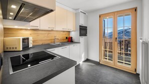 Cozinha moderna com fogão, micro-ondas e forno embutidos, uma janela grande com vista para as montanhas e uma porta de vidro deslizante.