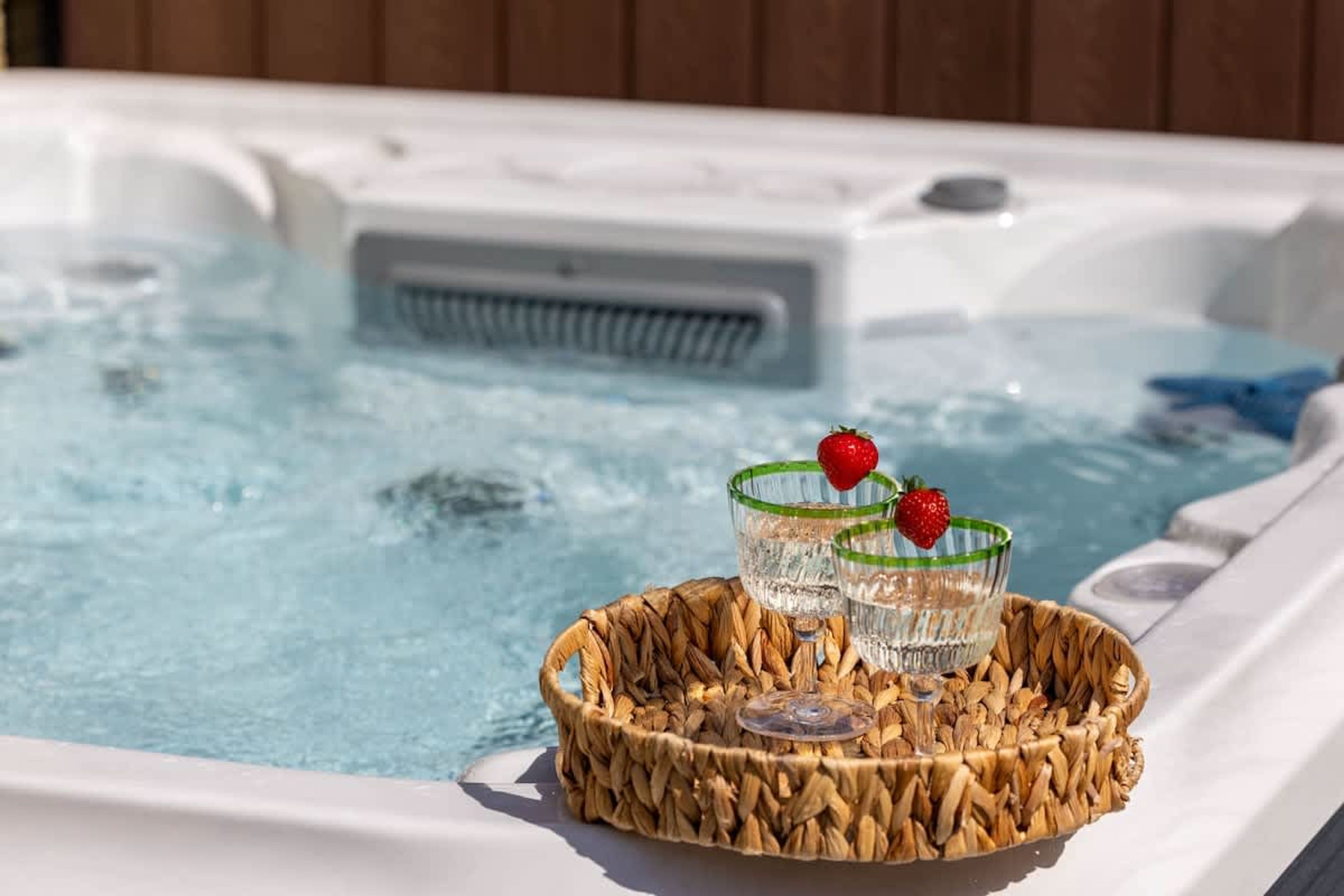 Un bain à remous avec un plateau en osier contenant deux verres d’eau et des fraises.