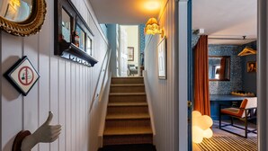 Eine Treppe führt zu einem Raum mit einem gemusterten Teppich, einer hängenden Leuchte und einem an der Wand befestigten Spiegel.