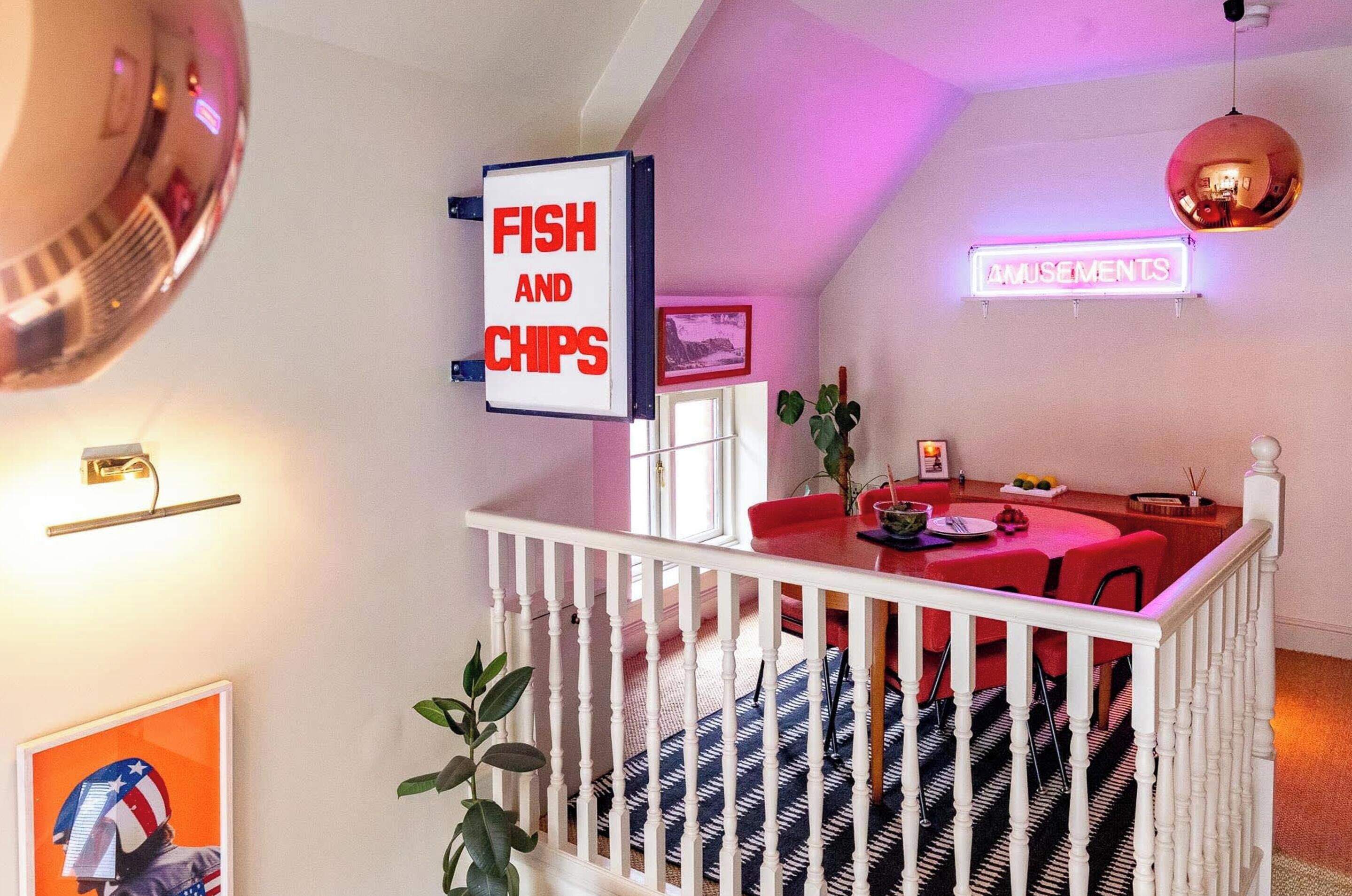 A dining area with a red table and chairs, a sign for 'Fish and Chips', and a neon sign for 'Amusements'.