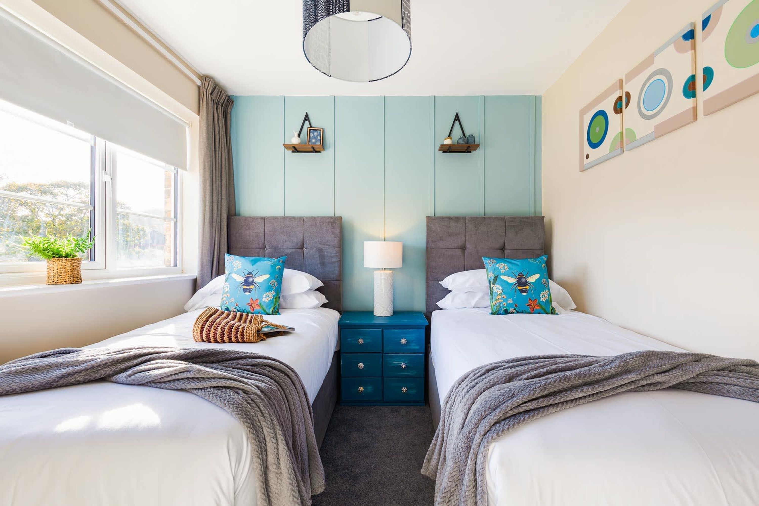 A bedroom with two beds, a nightstand, a lamp, and a window with a view.