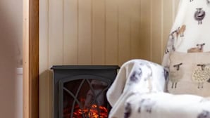 Ett mysigt rum med en vedeldad kamin, en fåtölj med en filt och träpanel på väggarna.