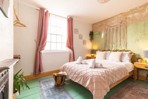 A bedroom with a bed, a dresser, a nightstand, a window with curtains, and a wall-mounted macrame piece. - The Little Blue Seaside House (Scarborough)