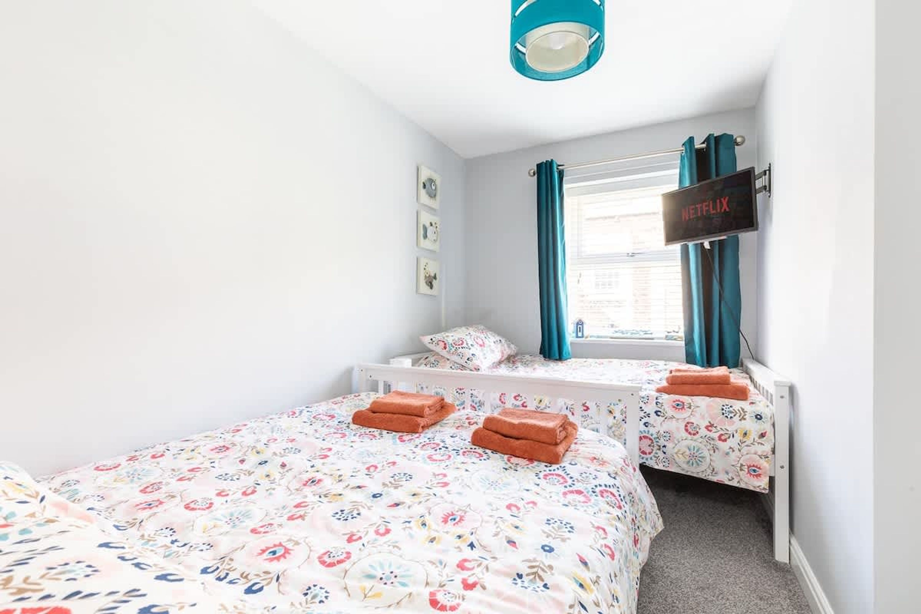 Un dormitorio con dos camas, una ventana con cortinas, un cartel de Netflix y una lámpara en el techo.