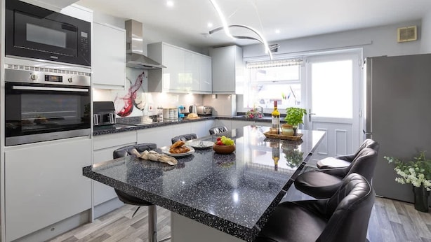 A modern kitchen with a central island, stainless steel appliances, and a dining area with leather chairs. - Townhouse Harbour Retreat (Scarborough)