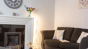 A living room with a fireplace, a sofa, a clock, and a vase with flowers. - Townhouse Harbour Retreat (Scarborough)