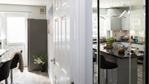 A modern kitchen with a central island, a refrigerator, and a dining area with a chair and a plant. - Townhouse Harbour Retreat (Scarborough)