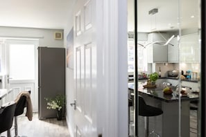 A modern kitchen with a central island, a refrigerator, and a dining area with a chair and a plant. - Townhouse Harbour Retreat (Scarborough)