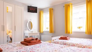 A hotel room with two beds, a TV mounted on the wall, a white dresser, and yellow curtains. - Townhouse Harbour Retreat (Scarborough)