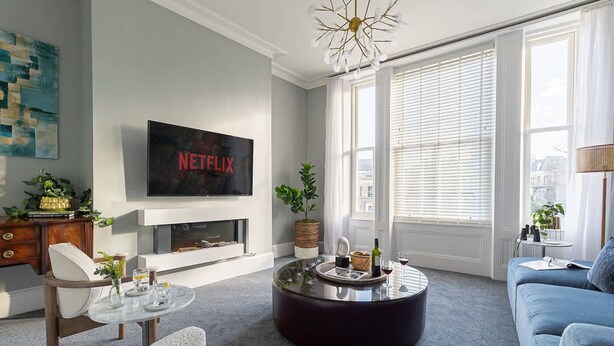 Uma sala de estar moderna com lareira, uma mesa de centro redonda, um sofá e uma televisão fixada na parede.