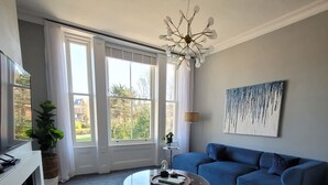 Uma sala de estar com um sofá azul, uma poltrona branca, uma mesa de centro e um quadro na parede.