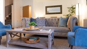 Uma sala de estar com um sofá cinzento, poltronas azuis, uma mesa de centro de madeira e um espelho na parede.