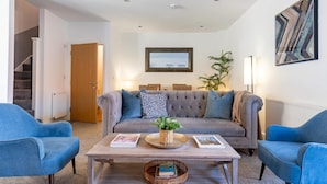 Uma sala de estar moderna com um sofá cinza, duas poltronas azuis, uma mesa de centro de madeira e um quadro na parede.