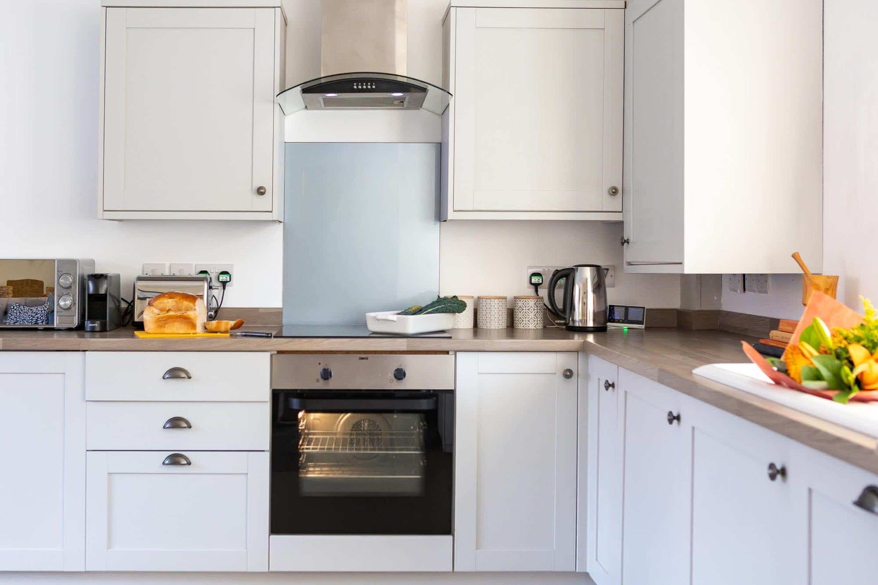 Una cucina moderna con mobili bianchi, forno integrato, macchina per il caffè e una ciotola di frutta sul piano di lavoro.