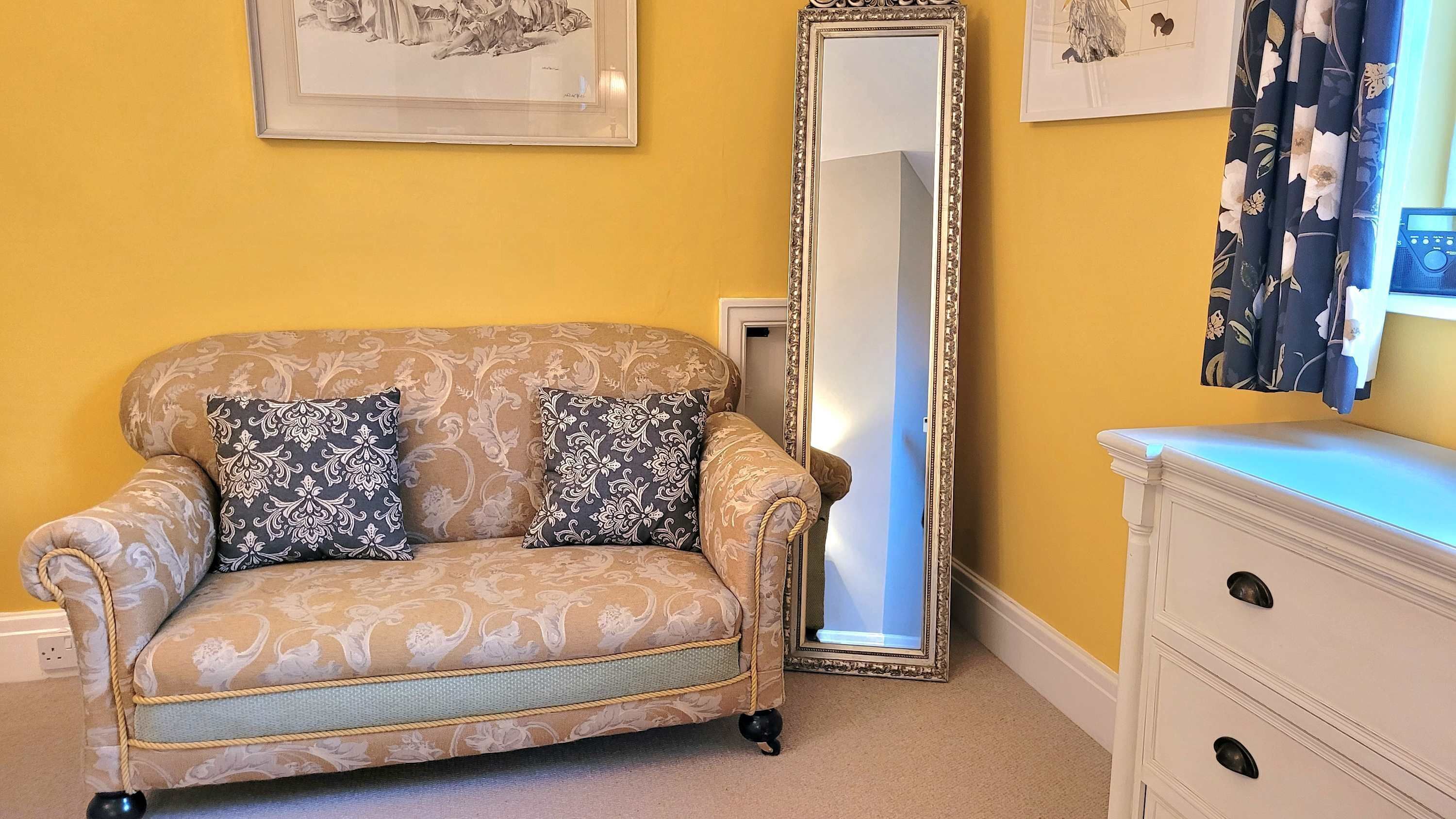 A room with a patterned sofa, a large mirror, a dresser, and a framed picture on the wall.