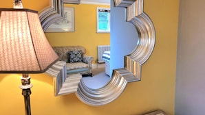 Ein Spiegel mit einem einzigartigen geometrischen Rahmen, der einen Raum mit einem Sofa, einem Heizkörper und einer Lampe widerspiegelt.