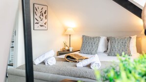 A neatly made bed with a grey blanket and two pillows, a bedside lamp, a small table with a plant, and a framed artwork on the wall. - Ocean Pearl - Seaside Sanctuary (Scarborough)