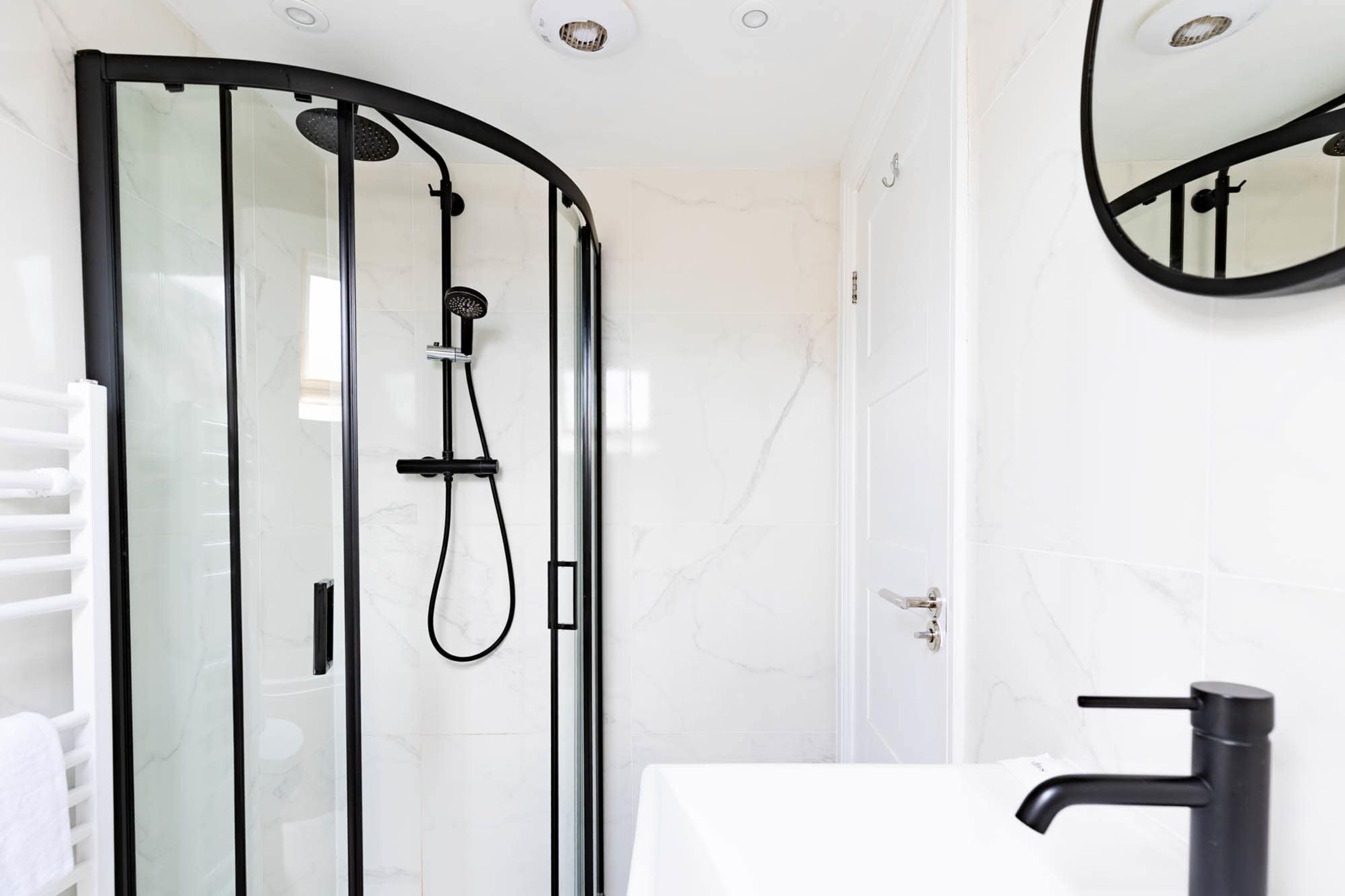 A modern bathroom with a glass-enclosed shower, a white sink, and a black faucet.