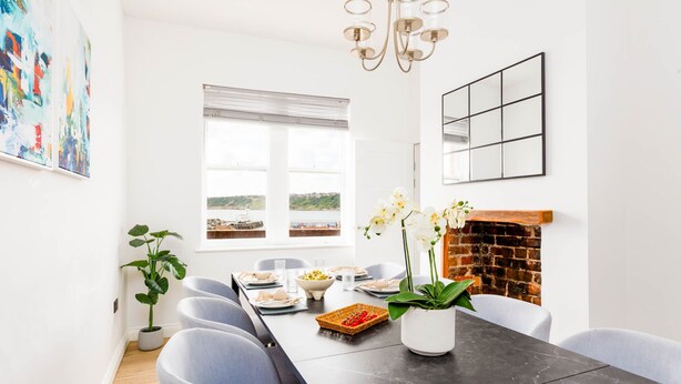 A dining area with a long table, chairs, a potted plant, and a fireplace. - Ocean Pearl - Seaside Sanctuary (Scarborough)