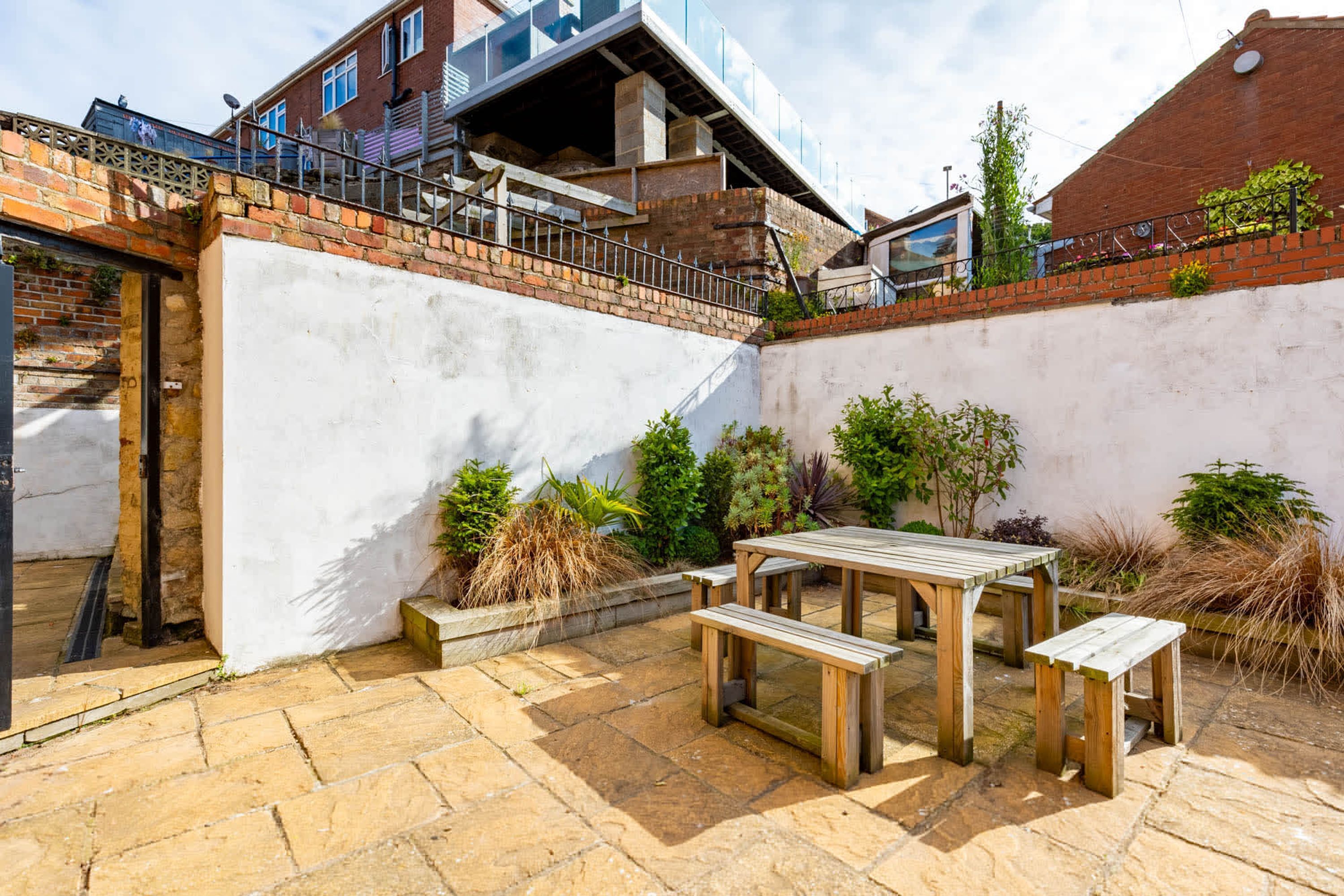 A courtyard with a stone patio, wooden benches, and a table.