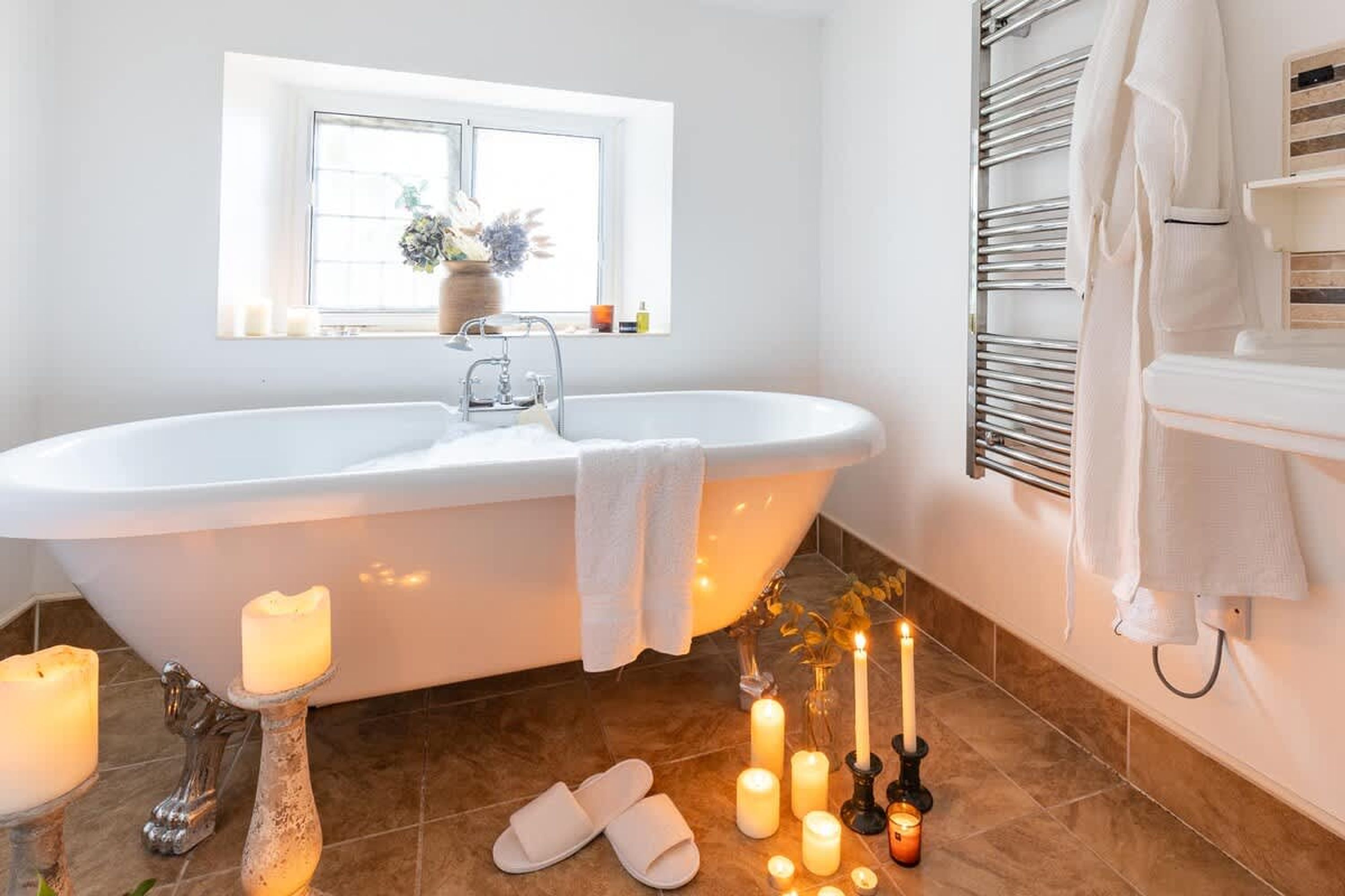 A modern bathroom with a freestanding bathtub, a window with a view, and multiple candles on the floor.
