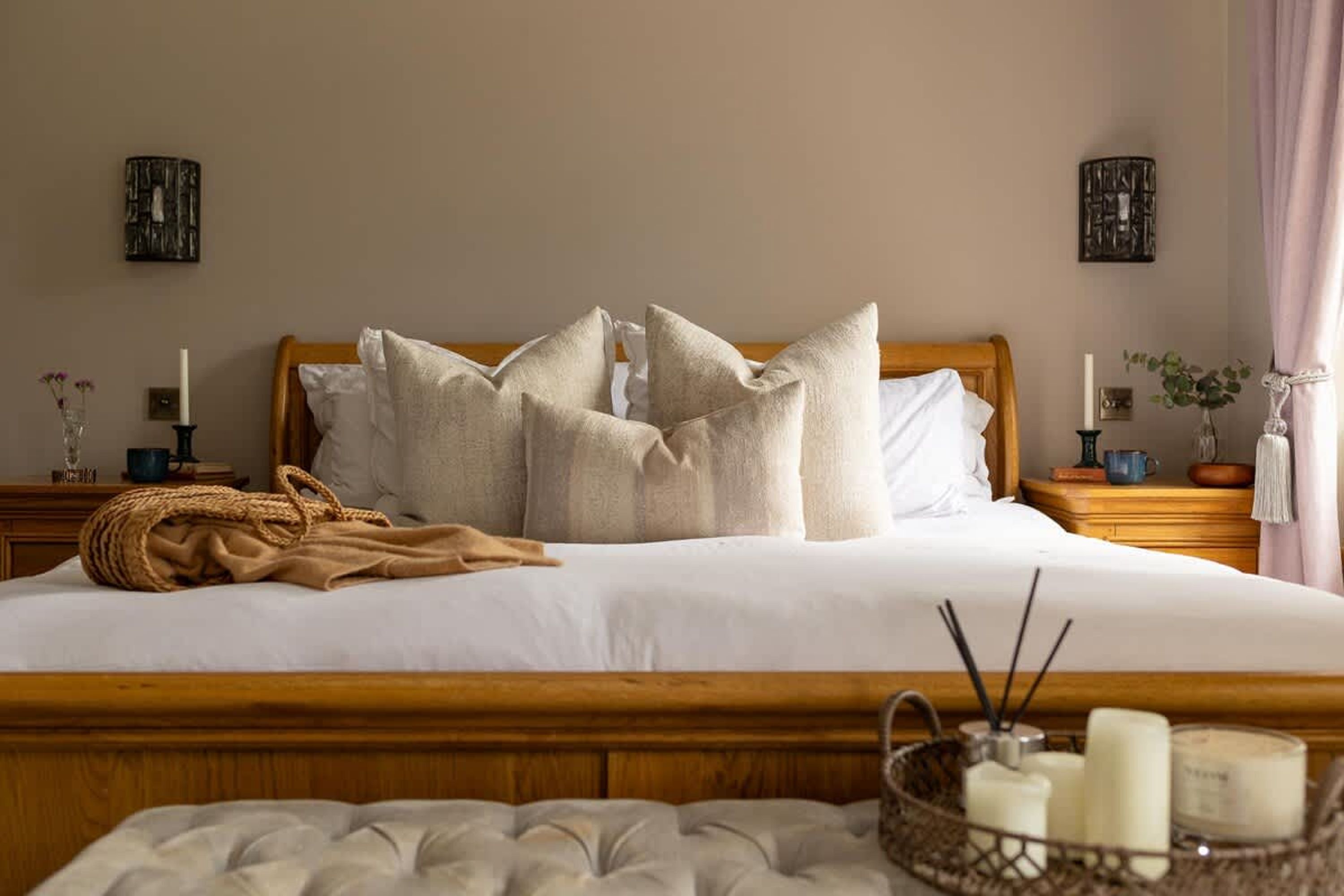 Un lit bien fait, avec une tête de lit en bois, une table de chevet sur laquelle est posée une bougie, et un élément décoratif mural.