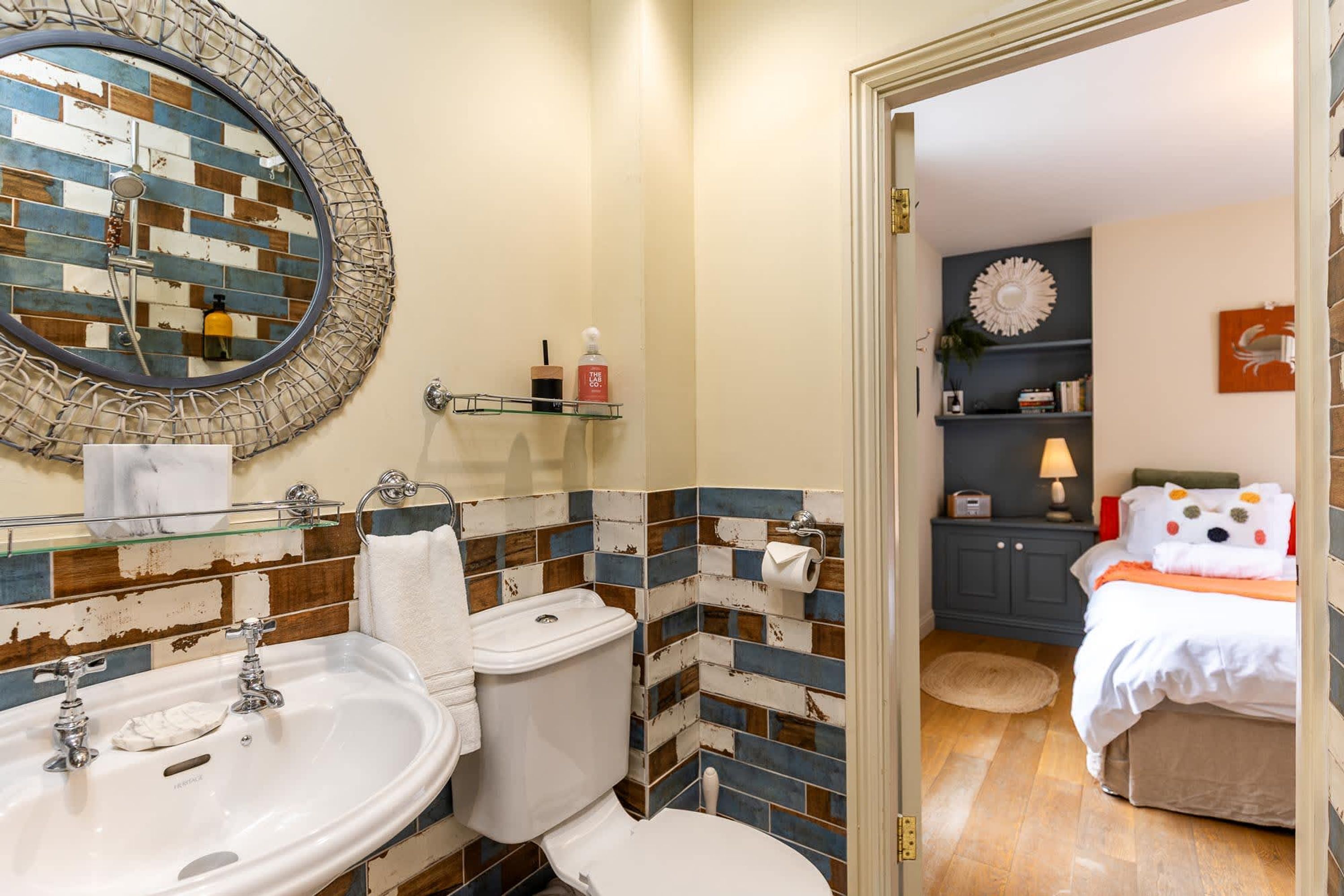 Bagno con doppio lavabo, WC e specchio con cornice decorativa. Si vede uno scaffale con articoli da toilette e un asciugamano appeso al muro.