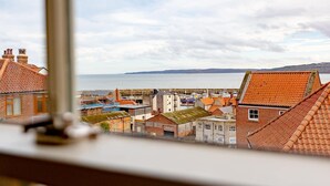 Une ville côtière aux toits traditionnels recouverts de tuiles rouges, dotée d’un port de plaisance et offrant une vue sur la mer.