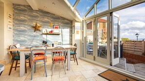 Un espace repas comprenant une table et des chaises, un mur décoré de motifs et une vue dégagée sur l’extérieur grâce à de grandes fenêtres.