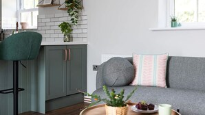 A modern kitchen with a green chair, a grey sofa with patterned pillows, and a tray with a plant and food items. - Ivy Mews - Converted Barn in Popular Village (Scarborough)