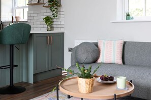 A modern kitchen with a green chair, a grey sofa with patterned pillows, and a tray with a plant and food items. - Ivy Mews - Converted Barn in Popular Village (Scarborough)