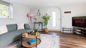 A living room with a sofa, coffee table, TV, and a door with a circular window. - Ivy Mews - Converted Barn in Popular Village (Scarborough)