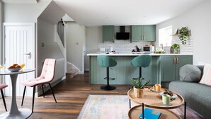 A modern kitchen with green cabinets, a white countertop, and a central island with bar stools. - Ivy Mews - Converted Barn in Popular Village (Scarborough)