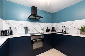 A modern kitchen with dark cabinets, a marble countertop, a built-in oven, a toaster, a coffee maker, and a sink. - Old Town House in Scarborough (Scarborough)