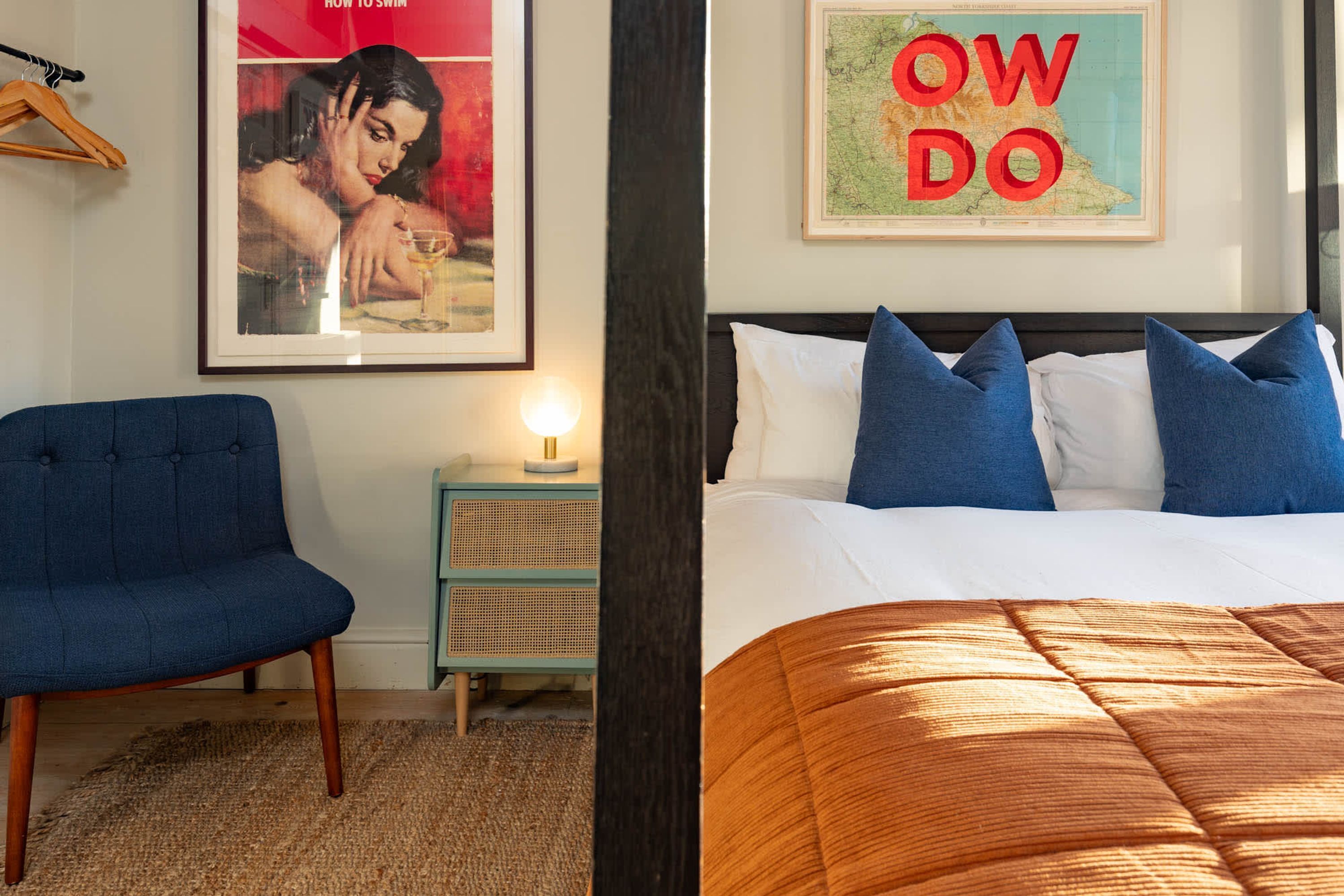 Ein Hotelzimmer mit Bett, Sessel, Nachttisch und einem Poster an der Wand.