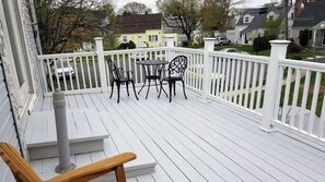 Une terrasse en bois peinte en blanc, avec une balustrade blanche, deux chaises et une table.
