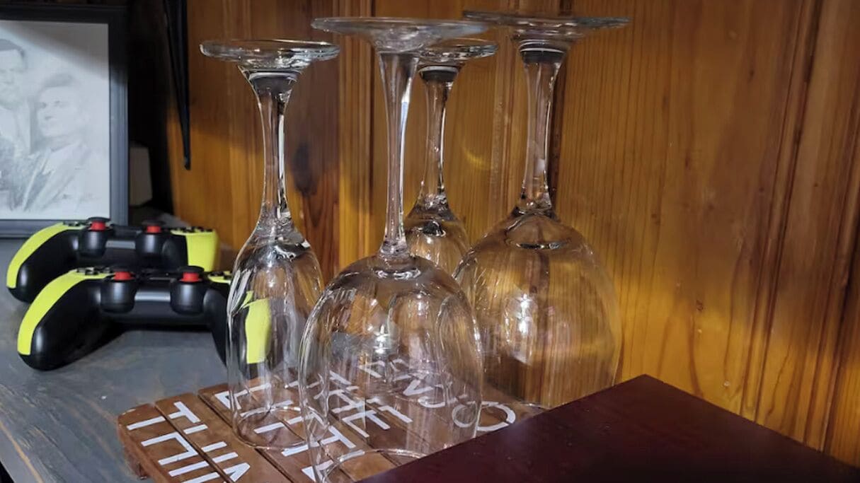 A wooden table with several clear wine glasses and a game controller.