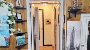 A hallway with wooden walls, a door at the end, and a framed picture of a building on the right. - Cozy 1-bedroom on the 2nd floor in Valley Stream, with a beautiful outdoor deck. (Valley Stream)
