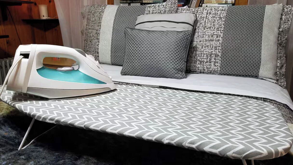 An ironing board with an iron and a patterned bedspread.