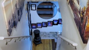 A staircase with a wooden floor, a black object at the bottom, and a wall with framed pictures and a mirror. - Cozy 1-bedroom on the 2nd floor in Valley Stream, with a beautiful outdoor deck. (Valley Stream)