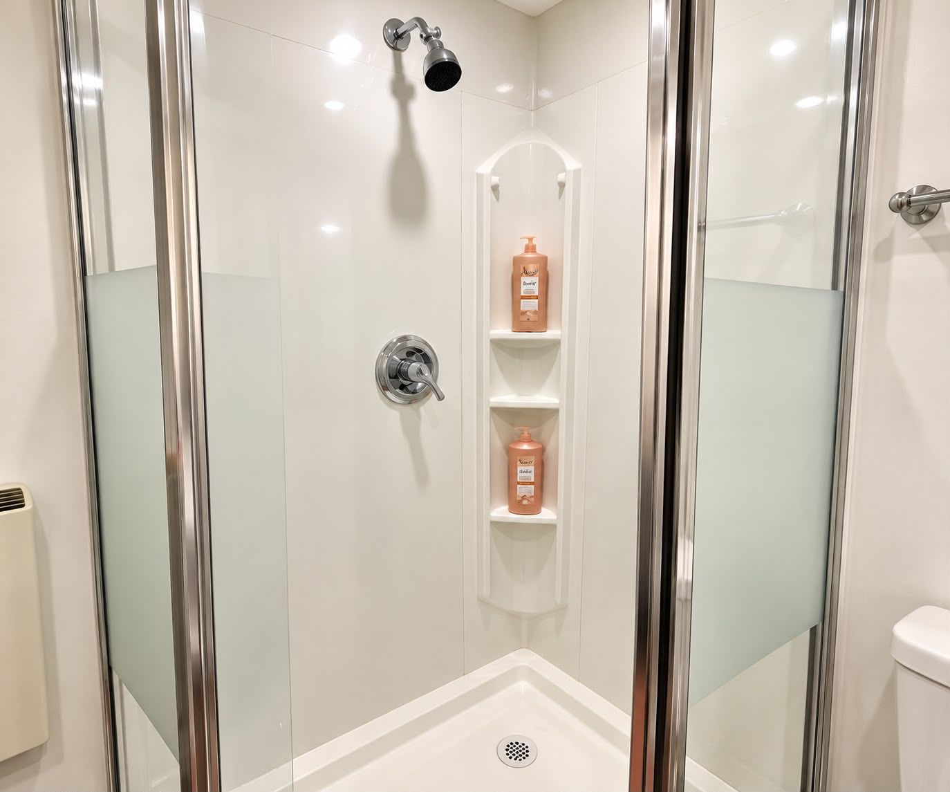 Une cabine de douche moderne dotée d’une porte en verre, d’un pommeau de douche à main et d’une étagère pour les articles de toilette.