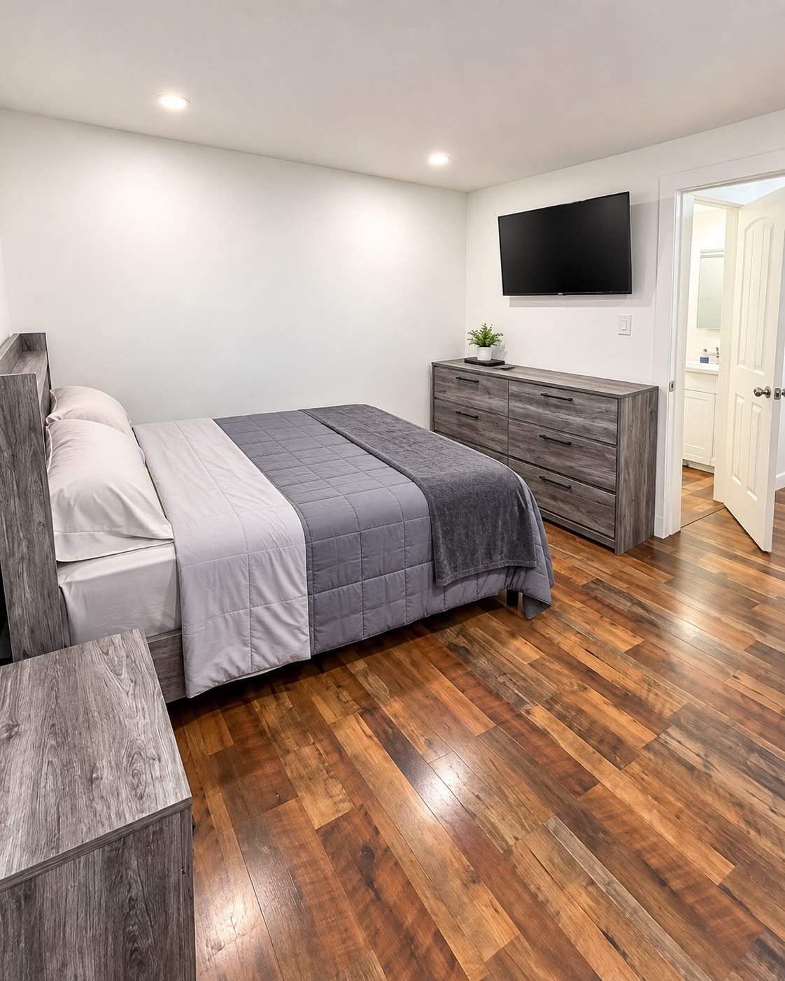 A modern bedroom with a bed, dresser, and TV.