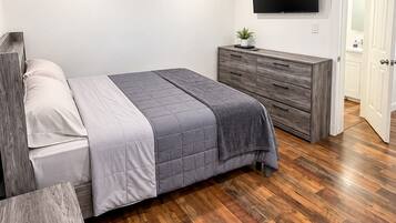 A modern bedroom with a bed, dresser, and TV.