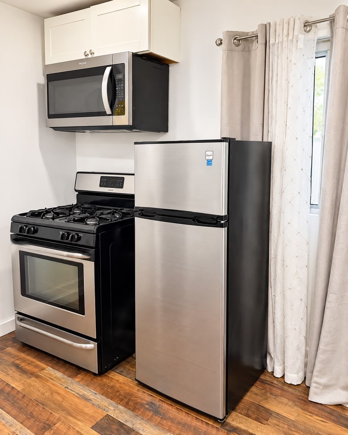 A compact kitchen with a stainless steel refrigerator, a built-in oven, and a microwave.