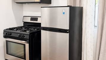 A compact kitchen with a stainless steel refrigerator, a built-in oven, and a microwave.